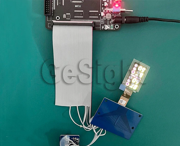 flexible AMOLED demo setup connected to an MCU board via ribbon cable, screen showing test pattern.