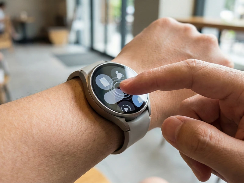 Close-up of a finger tapping a round smartwatch touch interface on a wrist, demonstrating touch screen interaction.